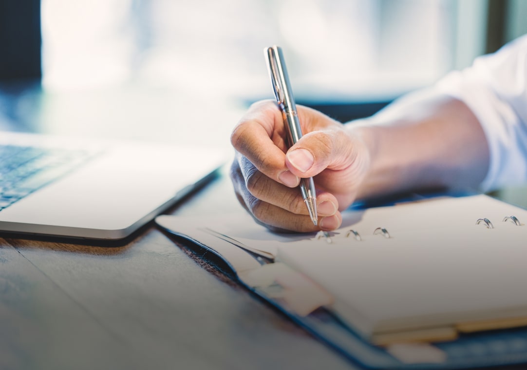 main tenants un stylo sur un carnet posé sur un bureau
