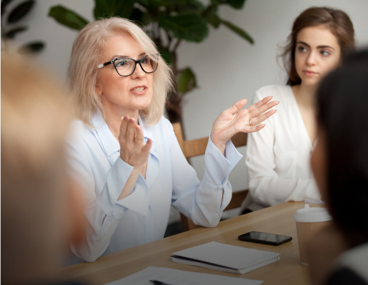 une femme assise à une table s'adresse à des individus assis autour d'elle